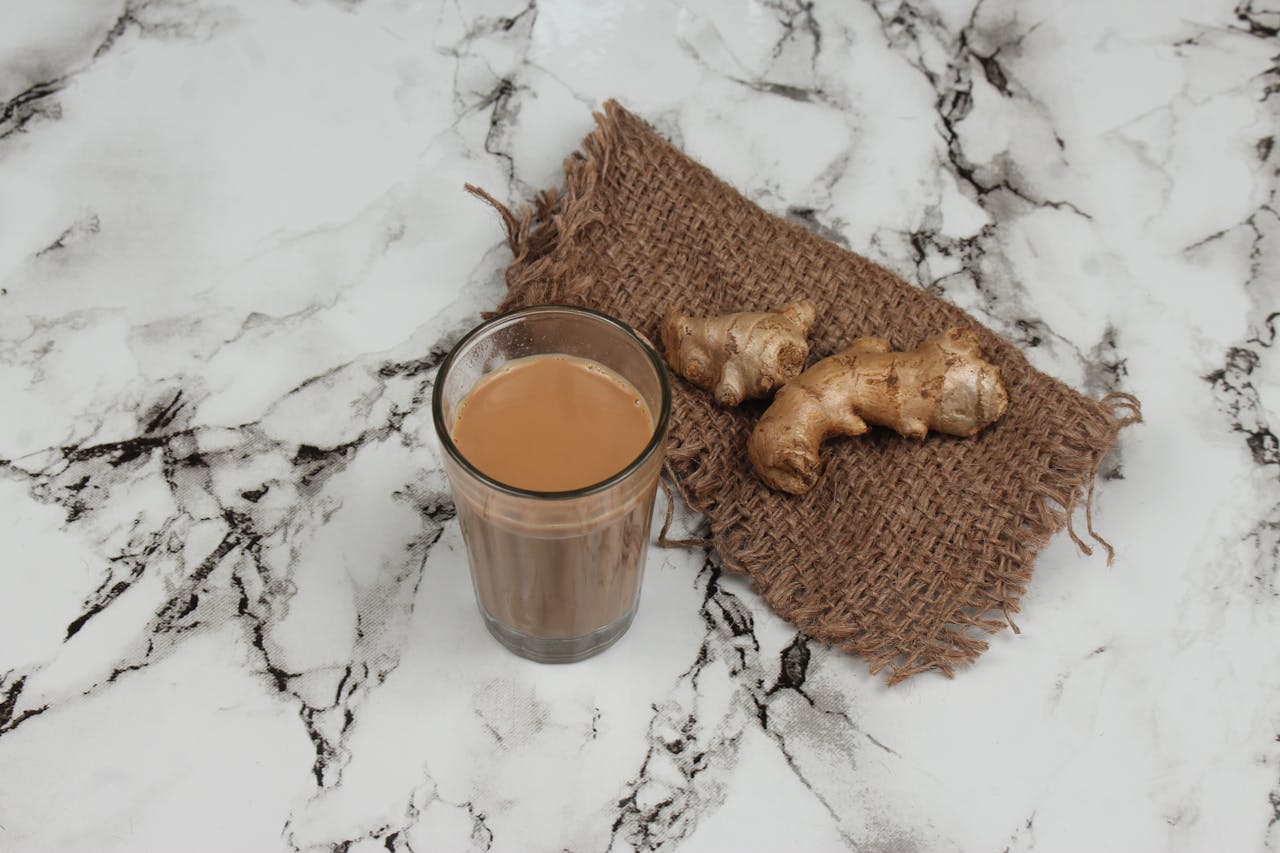 A glass of traditional Indian masala chai served with fresh ginger on a marble countertop.